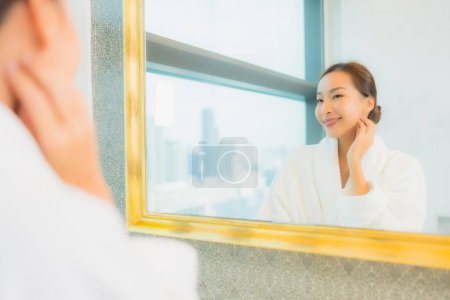 Foto de Retrato hermosa joven asiática mujer comprobar hasta su cara en espejo en baño interior - Imagen libre de derechos