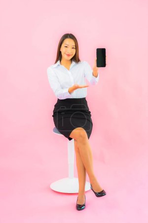 Foto de Retrato hermosa joven asiática mujer uso inteligente móvil en rosa aislado fondo - Imagen libre de derechos