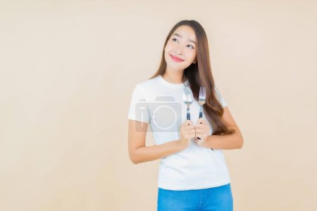 Téléchargez les photos : Portrait belle jeune femme asiatique avec cuillère et fourchette sur fond de couleur crème - en image libre de droit