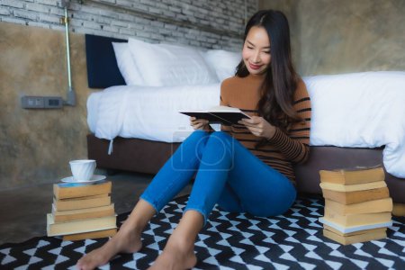 Foto de Joven mujer asiática con taza de café y leer libro en la cama en el interior del dormitorio - Imagen libre de derechos