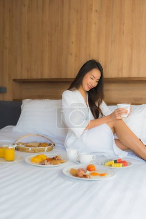 Foto de Retrato hermosa joven mujer asiática feliz disfrutar con el desayuno en la cama en el interior del dormitorio - Imagen libre de derechos