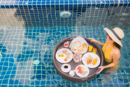 Foto de Retrato hermosa joven asiática mujer feliz sonrisa relajarse con el desayuno flotando alrededor de la piscina en el complejo hotelero - Imagen libre de derechos