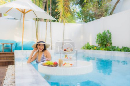 Téléchargez les photos : Portrait belle jeune femme asiatique profiter avec thé après-midi ou petit déjeuner flottant sur la piscine dans la station hôtelière - en image libre de droit