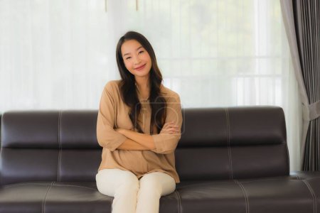 Foto de Retrato hermosa joven asiática mujer feliz sonrisa relajarse en sofá en sala de estar interior - Imagen libre de derechos