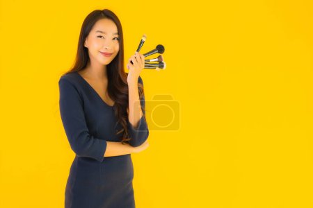 Foto de Retrato hermosa joven asiática mujer con maquillaje cepillo en amarillo aislado fondo - Imagen libre de derechos