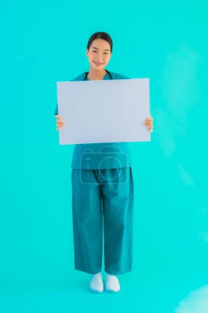 Téléchargez les photos : Portrait belle jeune femme asiatique médecin avec carton vide pour l'espace de copie sur fond bleu isolé - Soins de santé à l'hôpital et concept de clinique - en image libre de droit