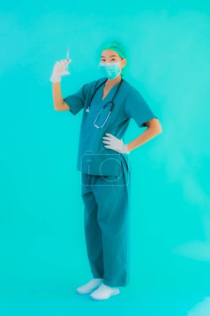Foto de Retrato hermosa joven asiática médico mujer usar máscara con jeringa vacuna para proteger de covid19 o coronavirus en azul aislado fondo - Imagen libre de derechos