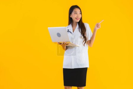 Photo for Portrait beautiful young asian doctor woman use notebook or laptop on yellow isolated background - Royalty Free Image