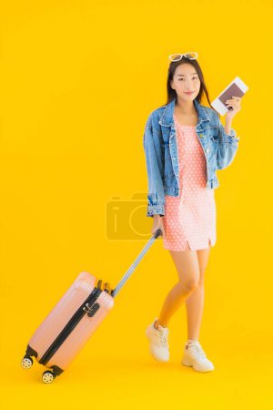 Foto de Retrato hermosa joven asiática mujer con equipaje bolsa de viaje con pasaporte y billete de embarque en amarillo aislado fondo - Imagen libre de derechos