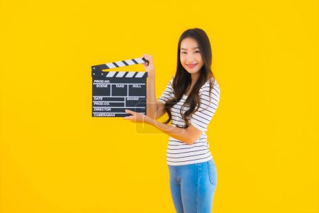 Foto de Retrato hermosa joven asiática mujer show clapper película tablero en amarillo aislado fondo - Imagen libre de derechos