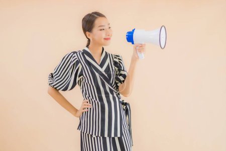 Téléchargez les photos : Portrait belle jeune femme asiatique avec mégaphone sur fond brun - en image libre de droit