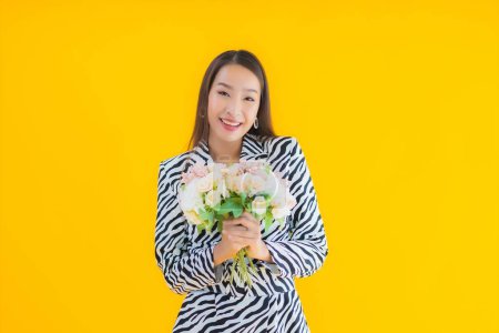 Foto de Retrato hermosa joven asiática mujer sonrisa feliz con flor en amarillo aislado fondo - Imagen libre de derechos