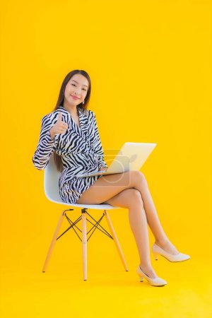 Foto de Retrato hermosa joven mujer asiática uso ordenador portátil en amarillo aislado fondo - Imagen libre de derechos