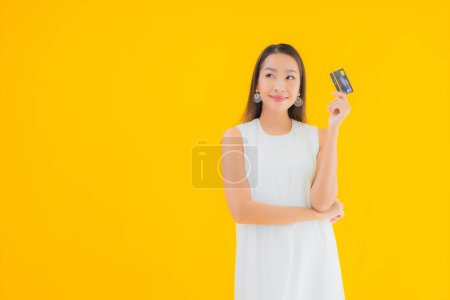 Téléchargez les photos : Portrait belle jeune femme asiatique avec carte de crédit pour les achats en ligne sur fond jaune isolé - en image libre de droit