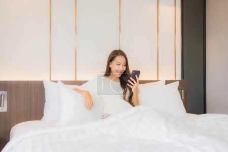Foto de Retrato hermosa joven mujer asiática uso inteligente teléfono móvil en la cama en el interior del dormitorio - Imagen libre de derechos