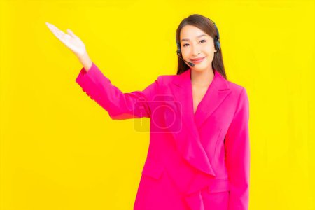 Foto de Retrato hermosa mujer asiática joven con auriculares y auriculares para el contacto del centro de llamadas sobre fondo amarillo - Imagen libre de derechos