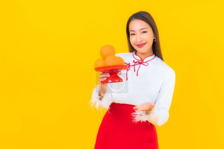 Téléchargez les photos : Portrait belle jeune femme asiatique avec des fruits orange sur fond jaune - en image libre de droit