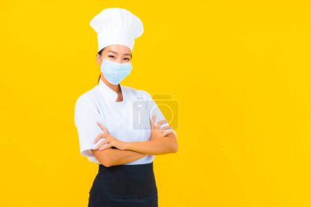 Téléchargez les photos : Portrait belle jeune femme asiatique chef porter un masque pour protéger covid19 ou coronavirus sur fond isolé jaune - en image libre de droit