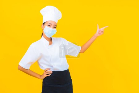 Photo for Portrait beautiful young asian woman chef wear mask for protect covid19 or coronavirus on yellow isolated background - Royalty Free Image