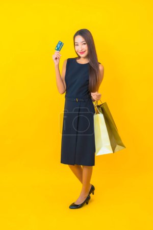 Téléchargez les photos : Portrait belle jeune femme d'affaires asiatique avec beaucoup de sac à provisions sur fond jaune - en image libre de droit