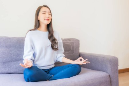 Téléchargez les photos : Portrait belle jeune femme asiatique méditation sur canapé dans le salon intérieur - en image libre de droit