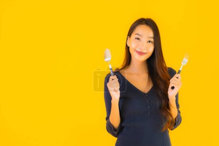 Téléchargez les photos : Portrait belle jeune femme asiatique avec cuillère et fourchette prête à manger sur fond jaune isolé - en image libre de droit