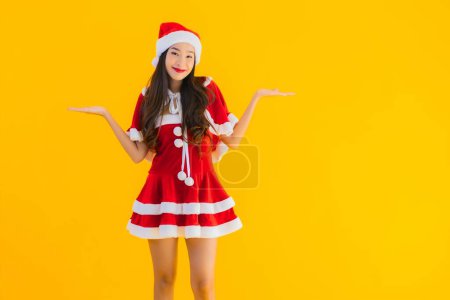 Photo for Portrait beautiful young asian woman christmas clothes and hat smile happy with other action on yellow isolated background - Royalty Free Image