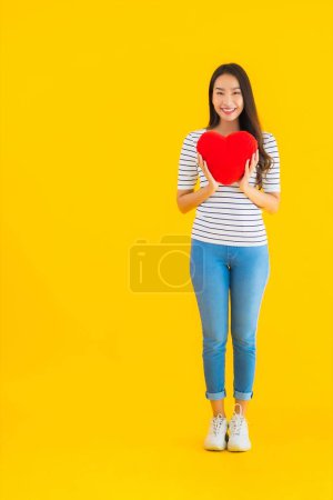 Photo for Portrait beautiful young asian woman show heart pillow on yellow isolated background - Royalty Free Image