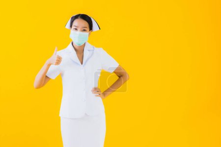 Téléchargez les photos : Portrait belle jeune femme asiatique thai infirmière porter un masque pour protéger covid19 ou coronavirus et montrer gel d'alcool sur fond isolé jaune - en image libre de droit