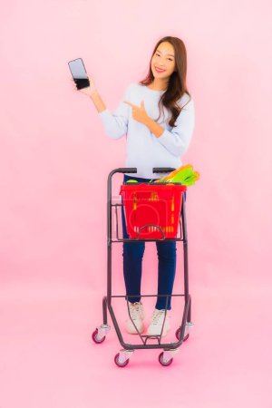 Téléchargez les photos : Portrait belle jeune femme asiatique avec fruits légumes et épicerie dans le panier sur fond rose isolé - en image libre de droit
