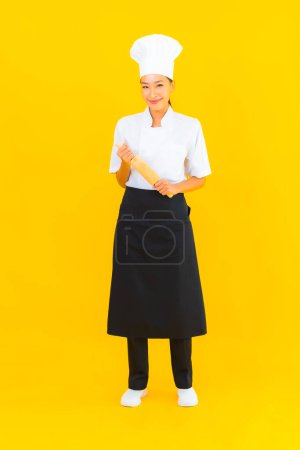 Téléchargez les photos : Portrait belle jeune femme asiatique chef avec rouleau à pâtisserie sur fond jaune isolé - en image libre de droit