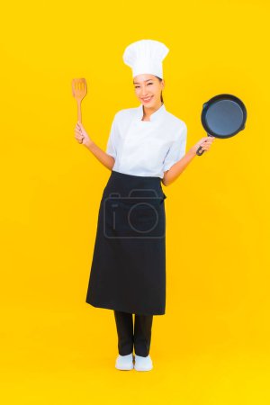 Photo for Portrait beautiful young asian chef woman with black pan on yellow isolated background - Royalty Free Image