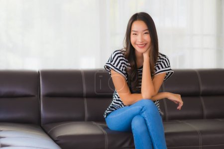Téléchargez les photos : Portrait belle jeune femme asiatique sourire heureux se détendre sur le canapé dans le salon intérieur - en image libre de droit