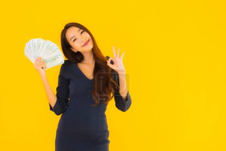 Foto de Retrato hermosa joven asiática mujer con dinero y dinero en efectivo en amarillo aislado fondo - Imagen libre de derechos