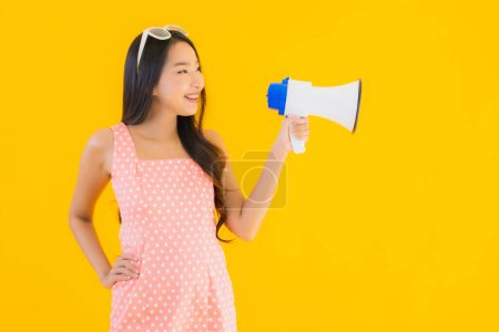 Téléchargez les photos : Portrait belle jeune femme asiatique parler fort avec mégaphone sur fond jaune isolé - en image libre de droit