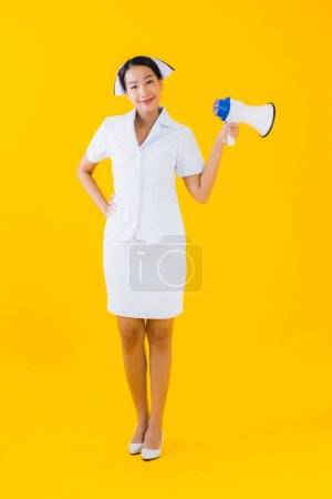 Photo for Portrait beautiful young asian woman thai nurse with megaphone for communicate in clinic and hospital on yellow isolated background - Royalty Free Image
