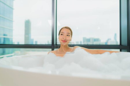 Foto de Retrato hermosa joven asiática mujer relajarse sonrisa ocio en bañera en baño interior - Imagen libre de derechos