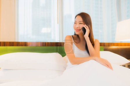Téléchargez les photos : Portrait belle jeune femme asiatique utiliser téléphone mobile intelligent sur le lit dans la chambre à coucher intérieur - en image libre de droit