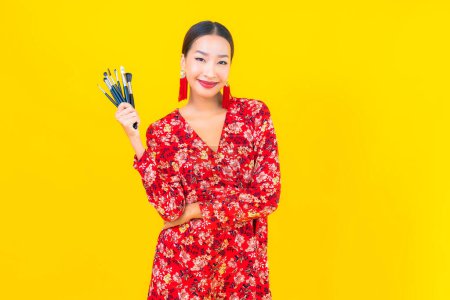 Photo for Portrait beautiful young asian woman with make up brush and cosmetic on yellow background - Royalty Free Image