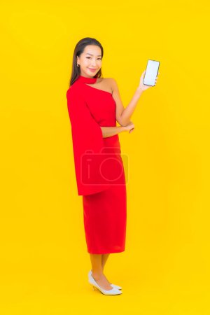 Photo for Portrait beautiful young asian woman with smart mobile phone with credit card on yellow background - Royalty Free Image