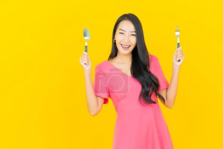 Photo for Portrait beautiful young asian woman smile with spoon and fork on yellow color background - Royalty Free Image