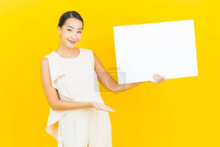 Téléchargez les photos : Portrait belle jeune femme asiatique avec panneau blanc vide sur fond de couleur jaune - en image libre de droit