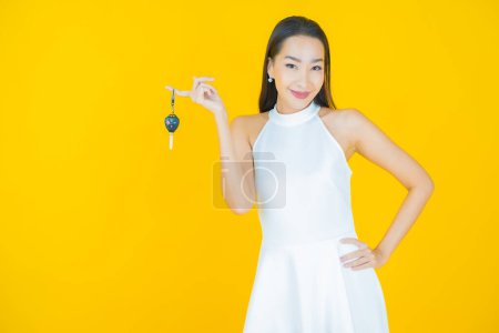 Téléchargez les photos : Portrait belle jeune femme asiatique sourire avec clé de voiture sur fond de couleur jaune - en image libre de droit