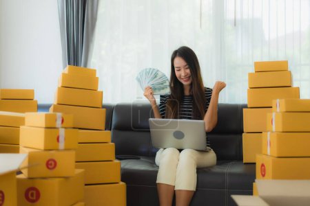 Foto de Retrato hermosa mujer asiática joven con envase de cartón paquete caja de embalaje prepararse para el envío para el cliente en línea de compras en la sala de estar - Imagen libre de derechos