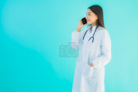 Téléchargez les photos : Portrait belle jeune asiatique médecin femme utiliser téléphone portable intelligent pour la clinique ou l'hôpital sur fond bleu isolé - en image libre de droit