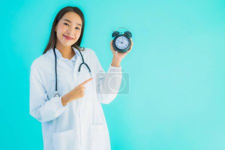 Foto de Retrato hermosa joven asiática médico mujer con reloj o alarma en azul aislado fondo - Imagen libre de derechos