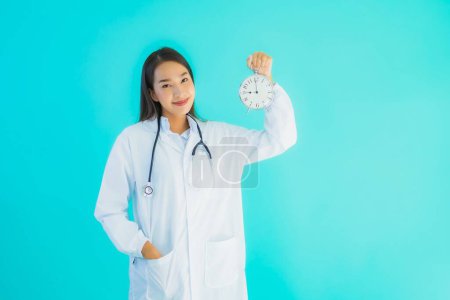 Téléchargez les photos : Portrait belle jeune asiatique médecin femme avec horloge ou alarme sur fond bleu isolé - en image libre de droit