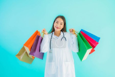Foto de Retrato hermosa joven asiática médico mujer con colorido bolso de compras de centro comercial en azul aislado fondo - Imagen libre de derechos