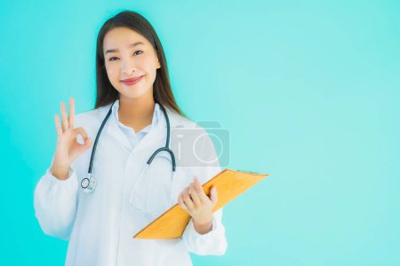 Foto de Retrato hermosa joven asiática médico mujer con tarjeta vacía cartel en azul aislado fondo - Imagen libre de derechos