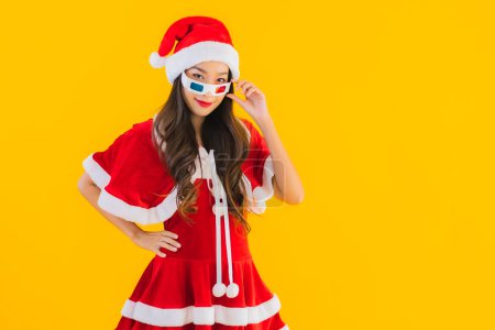 Téléchargez les photos : Portrait belle jeune femme asiatique porter des vêtements de Noël chapeau avec du maïs soufflé et des lunettes 3D prêt pour regarder le film sur fond jaune isolé - en image libre de droit